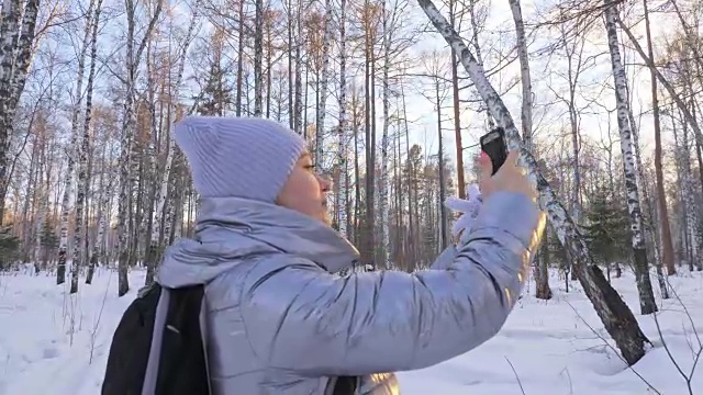 一个女人走在树林里。旅行者在森林里用手机拍照。女孩会自拍，用智能手机交流。美丽多汁的日落时分。视频素材