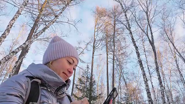 一个女人走在树林里。旅行者在森林里用手机拍照。女孩会自拍，用智能手机交流。美丽多汁的日落时分。视频素材