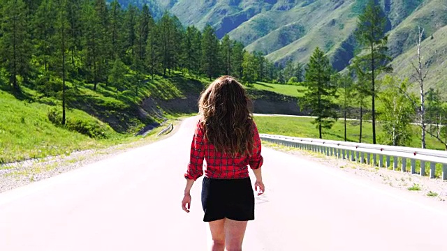 年轻女孩走在高速公路上。在群山的映衬下。这个女孩独自旅行。视频下载