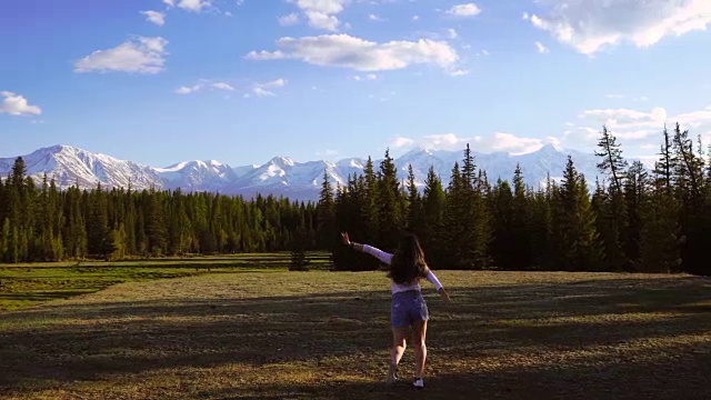 一个女孩在4k山的背景中沿着田野走着。视频素材