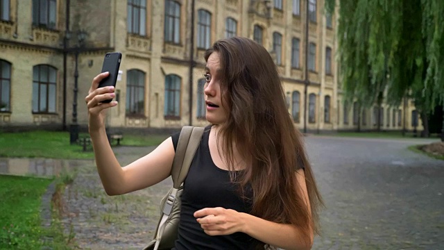 白种美女通过手机进行视频聊天和交谈，站在大学大楼附近的街道上视频素材