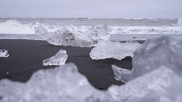 在Jokulsarlon Diamond的海滩上，海浪溅在冰岛黑沙滩上的冰山上的4K视频。视频素材