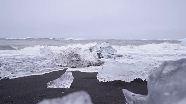 在Jokulsarlon Diamond的海滩上，海浪溅在冰岛黑沙滩上的冰山上的4K视频。视频素材