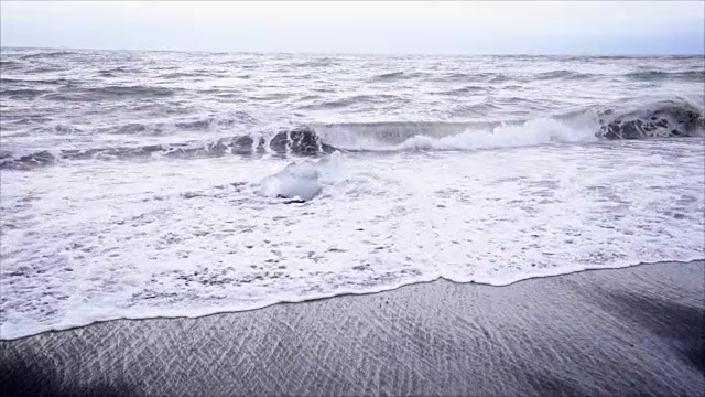 在Jokulsarlon Diamond的海滩上，海浪拍打在冰岛黑沙滩上的冰山的慢动作视频视频素材