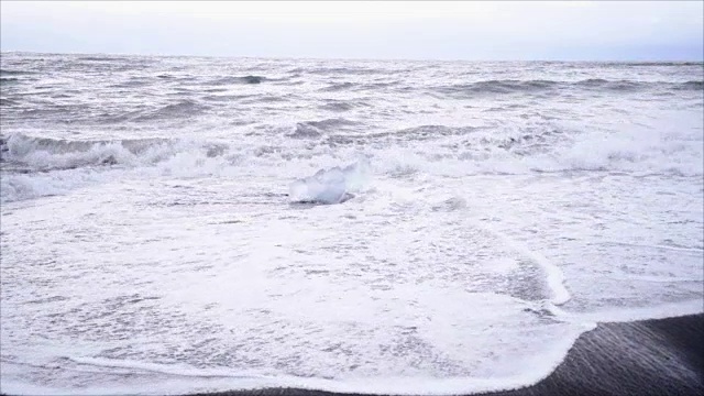 在Jokulsarlon Diamond的海滩上，海浪拍打在冰岛黑沙滩上的冰山的慢动作视频视频素材