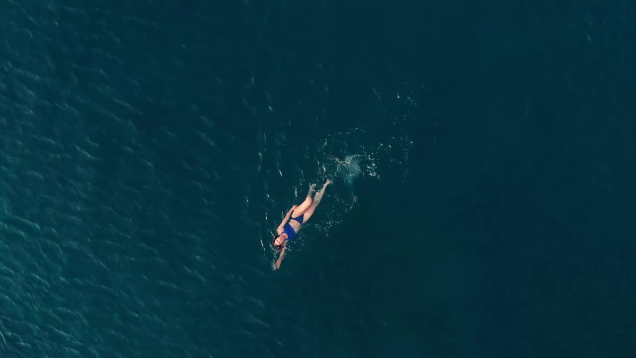 空中慢镜头:女子在湛蓝透明的海水中游泳视频素材