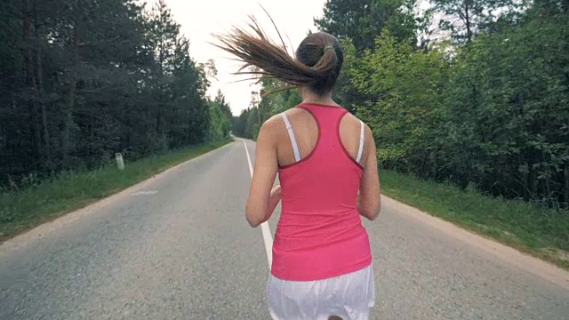 后视图的一个年轻的女士在良好的形状慢慢地沿着道路慢跑视频素材