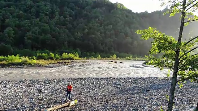 无人机镜头的摄影师旅行和拍照。地点:山区河流。摄影师用专业相机拍摄自然视频素材