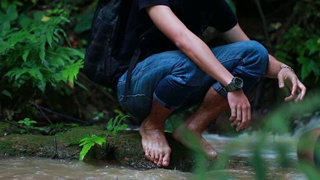 放松为生活的自然疗法概念:年轻人站在岩石上溪河快，走在水上放松。它天然药用，展现滋润宁静，清爽的泰国之旅视频素材