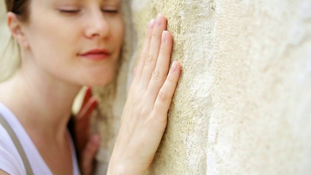 一个女人的手缓慢地靠在古老的石墙上。女性的手触摸岩石的粗糙表面视频素材