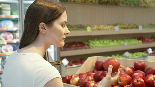 年轻女子在杂货店购买健康食品。素食女孩选择新鲜的红苹果视频素材