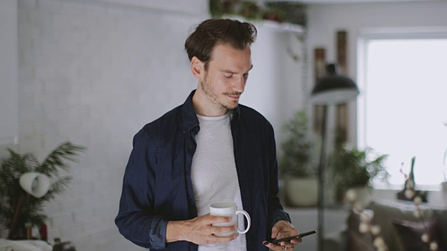 成年男性在厨房拿着一杯咖啡查看手机视频素材