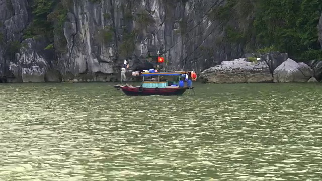 在下龙湾的悬崖底部，一艘越南渔船的中景视频素材