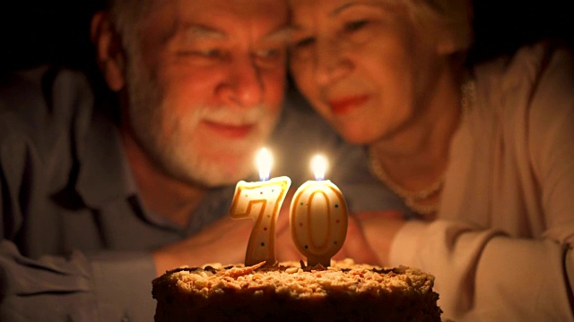 相爱的老年夫妇晚上在家用蛋糕庆祝结婚纪念日。吹灭蜡烛视频素材