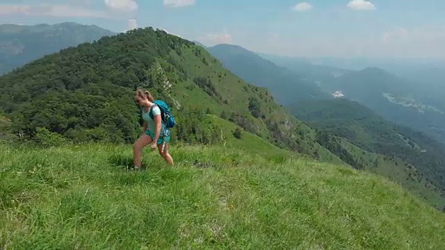 空中:活泼的女孩和她的狗爬上长满草的山，俯瞰绿色的山谷视频素材