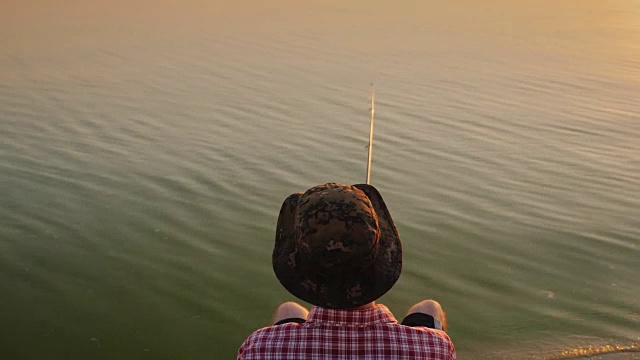 俯视图:一个戴着帽子的少年坐在湖边的椅子上，用钓竿钓鱼视频素材