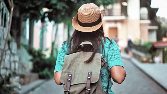 后视图活跃的徒步旅行者背包妇女在帽子走在舒适的欧洲城市狭窄的街道上视频素材