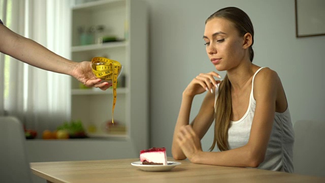 瘦骨嶙峋的女孩吃着蛋糕，手里拿着胶带，良心好像约着卡路里视频素材