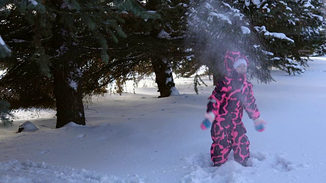 一个快乐的孩子穿着粉红色的衣服玩雪。视频素材