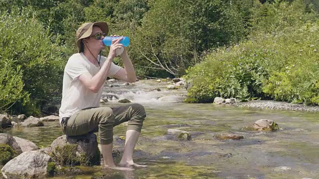 口渴的人从山涧里拿瓶水在露营时喝视频素材