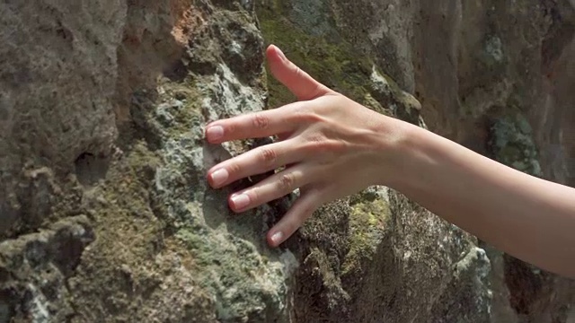 一个女人的手缓慢地靠在古老的石墙上。女性的手触摸岩石的粗糙表面视频素材