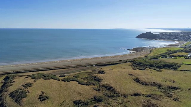 鸟瞰图，平移。无人机俯瞰草地、海滩、大海，以威尔士的克里斯西斯城堡和城镇为背景视频素材