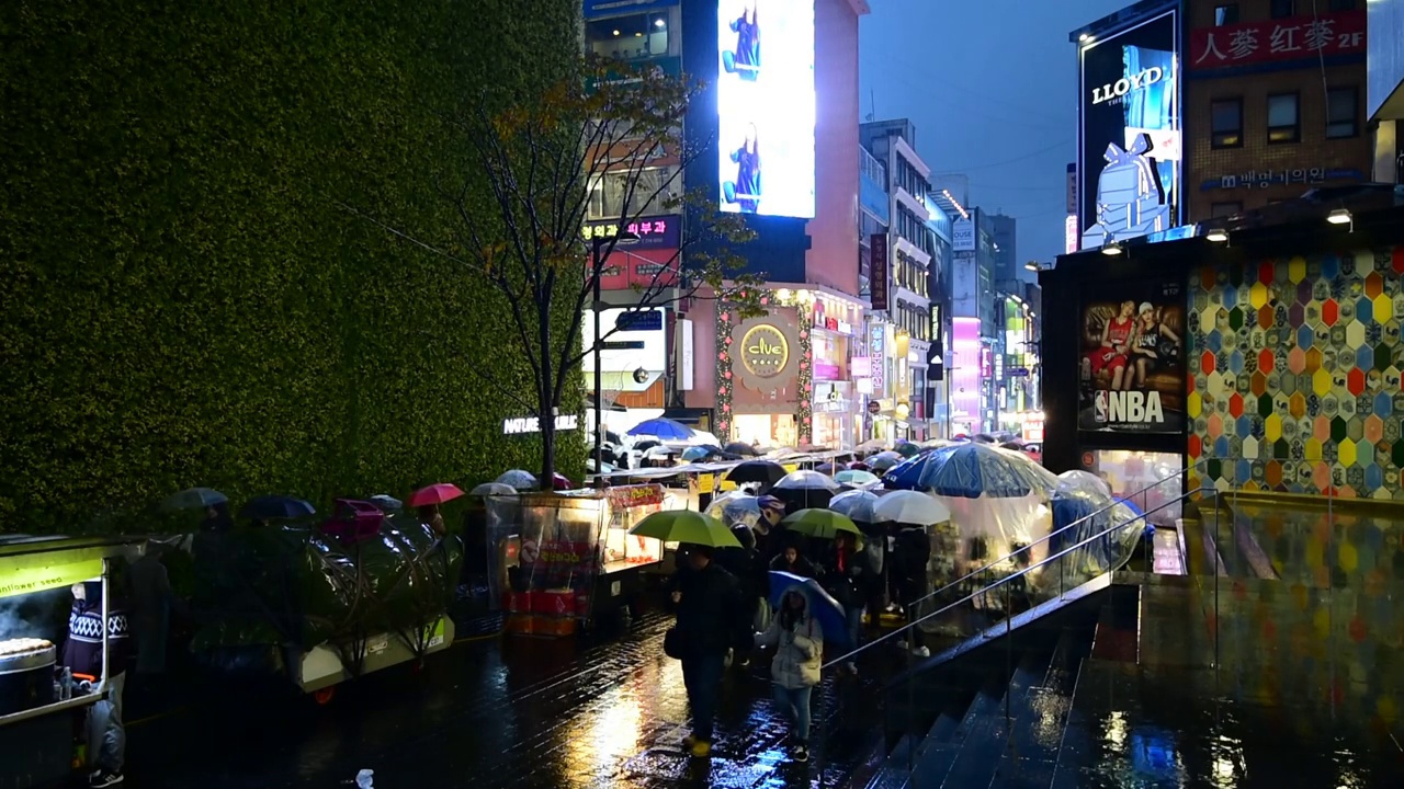 明洞的市场。在韩国首尔，人们在一个下雨天的夜晚撑着伞走在购物街上视频素材