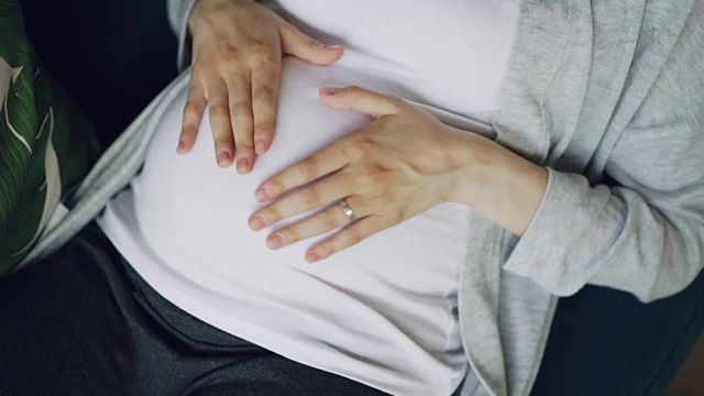 特写怀孕的肚子和温柔的女性的手爱抚和抚摸宝宝的肚子温柔和关怀，然后使心与手指象征爱的孩子。视频素材