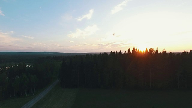 鸟瞰日落时瑞典田园诗般的风景。飞过松树林，湖泊和道路视频素材