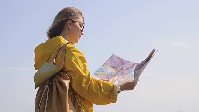 白种人女性徒步旅行者在黄色雨衣站在山上手里拿着地图的背影视频素材