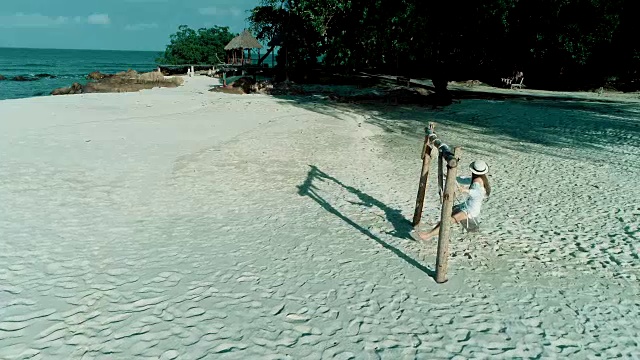 女人坐在沙滩上的秋千椅上，乌云密布的天空和美丽的沙滩沙滩背景。视频素材