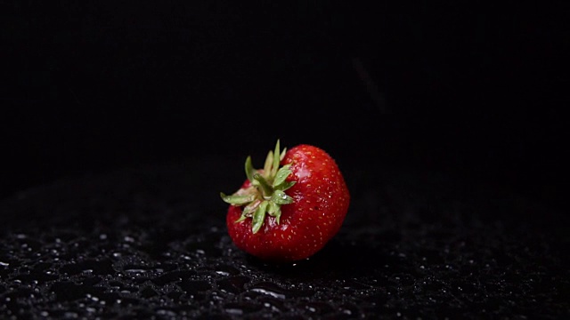 一个成熟的草莓与水滴旋转的黑色背景。视频素材