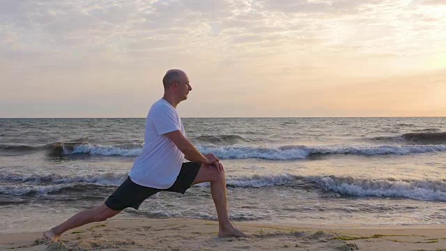 日出时在海浪中伸展腿的运动型男子视频素材