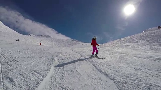 在一个阳光明媚的日子里，一名女子滑雪者在冬季山上的滑雪坡上滑雪视频素材