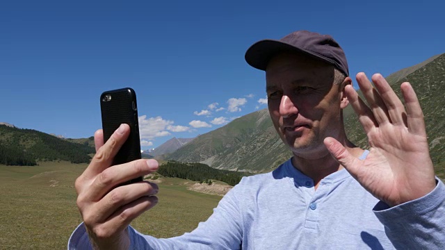 吉尔吉斯斯坦天山，一名戴着帽子的男子微笑着在电话上视频聊天视频素材