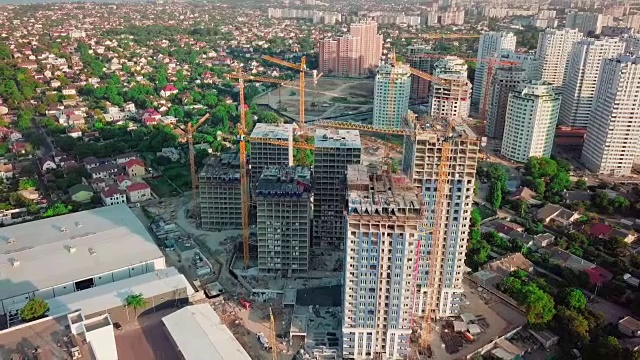 空中无人机。在大城市的发展中地区建设高层建筑。日落。在图片中，施工起重机和许多房屋正在建设中。广角镜头视频素材