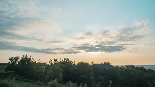 Timelaps日出。太阳在早晨升起时被记录下来，背景模糊。自然全景景观。天空中漂浮着云朵。太阳升起时照亮了云和树。视频素材