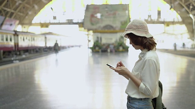 旅行家背包亚洲女人旅行在曼谷，泰国。快乐的年轻女性在火车站用智能手机聊天、阅读和发短信。视频素材