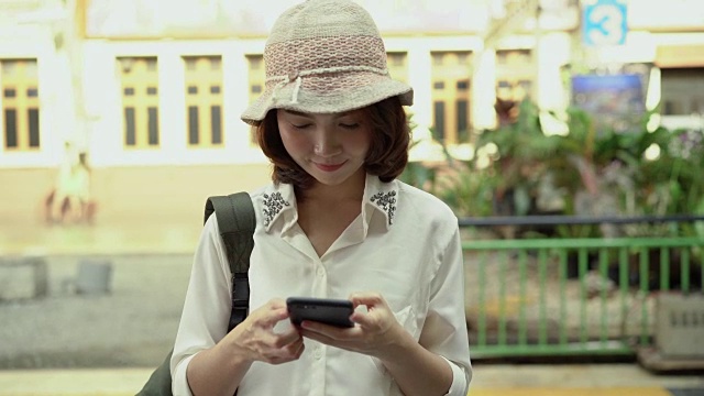 旅行家背包亚洲女人旅行在曼谷，泰国。快乐的年轻女性在火车站用智能手机聊天、阅读和发短信。视频素材