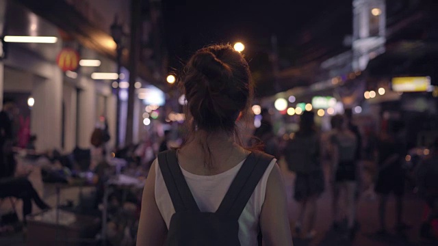 旅行家背包亚洲女人旅行在考山路在曼谷，泰国。快乐的年轻女性在惊人的地标假日旅行，享受她的旅程在夜晚的传统城市。视频素材