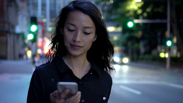 年轻女子拿着智能手机在夜里走在街上视频素材