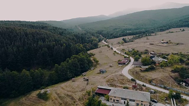 航拍与缓慢移动松树森林旁边的小山镇房子视频素材