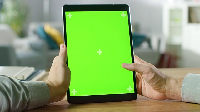 特写的人使用手势在绿色模拟屏幕数字平板电脑人像模式，而坐在他的办公桌。在舒适的客厅背景。视频素材
