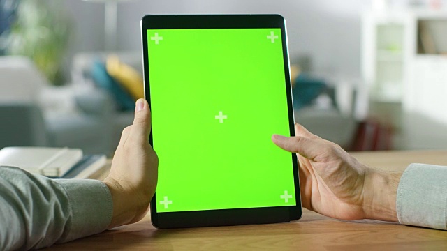 特写的人使用手势在绿色模拟屏幕数字平板电脑人像模式，而坐在他的办公桌。在舒适的客厅背景。视频素材