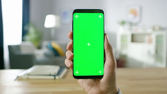 一个男人的特写持有绿色模拟屏幕智能手机和使用触摸屏手势。触摸手机色度键屏幕。在背景舒适的家庭气氛。视频素材