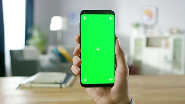 一个男人的特写持有绿色模拟屏幕智能手机和使用触摸屏手势。触摸手机色度键屏幕。在背景舒适的家庭气氛。视频素材