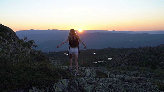 幸福的年轻女子在日落高山峻岭张开双手挥手视频素材