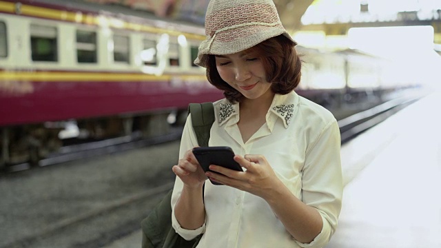 旅行家背包亚洲女人旅行在曼谷，泰国。快乐的年轻女性在火车站用智能手机聊天、阅读和发短信。视频素材