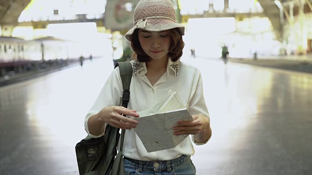 旅行家背包亚洲女人旅行在曼谷，泰国。快乐的年轻女性方向和看位置地图在火车站旅行前。视频素材