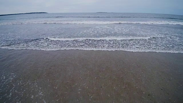 无人机的慢镜头海浪到达海岸的白色海洋泡沫空沙纹理。视频是从头顶的角度拍摄的视频素材